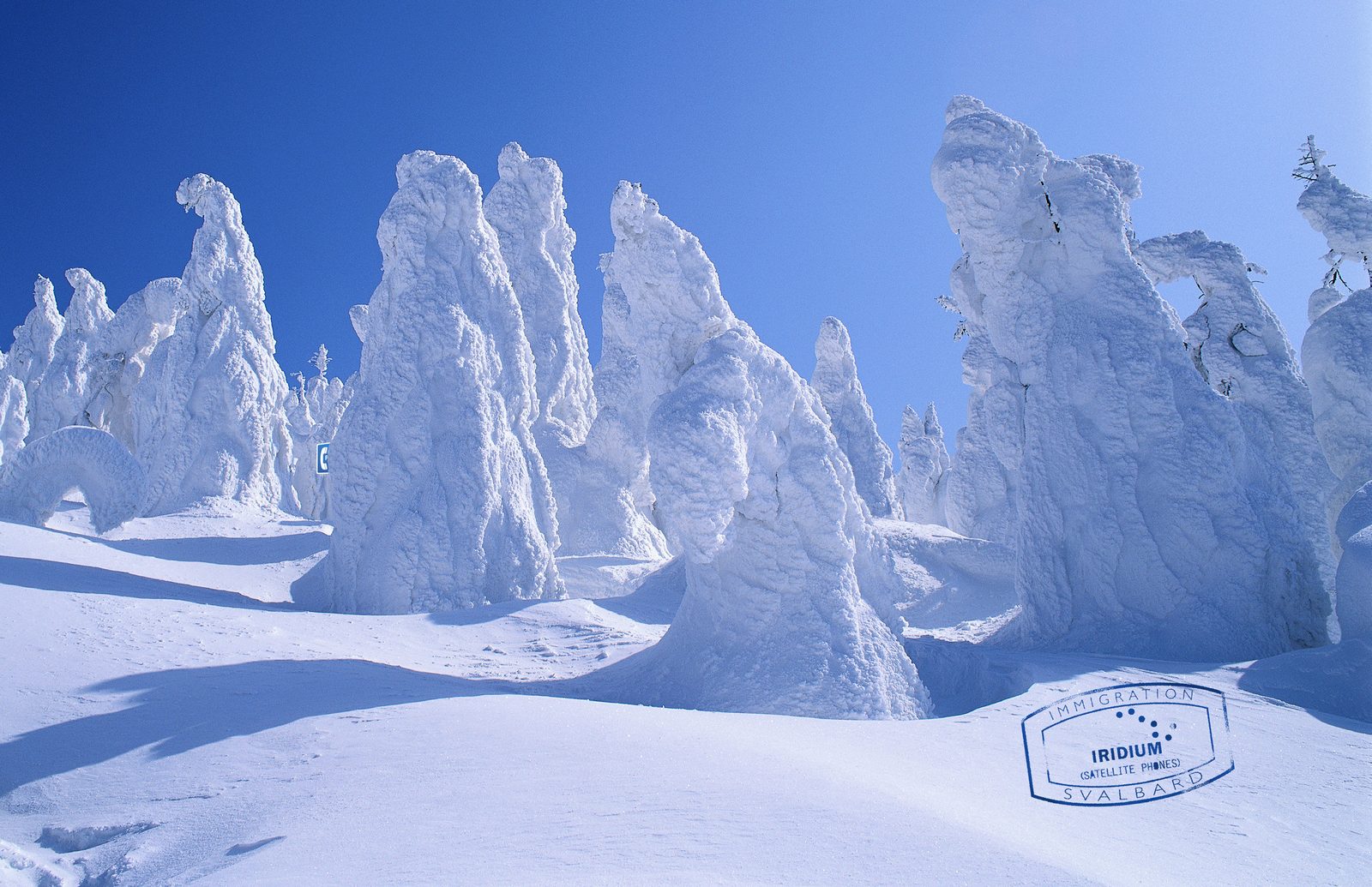 Iridium print ad: a blue Svalbard immigration stamp for Iridium Satellite Phones on wind-carved snow formations