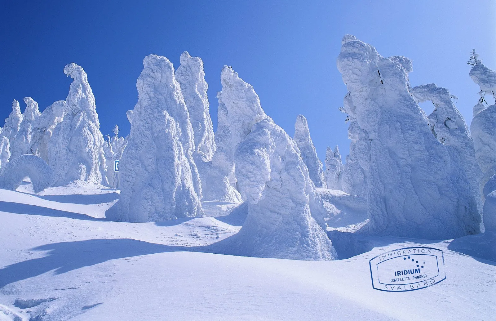 Iridium print ad: a blue Svalbard immigration stamp for Iridium Satellite Phones on wind-carved snow formations